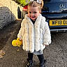 black_car, black_shoes, car, child, fur_coat, hair_bows, license_plate, mercedes, outdoor, pavement, plush_toy, shadow, skirt, smile, stone_wall, sunny, tights, toddler, white_coat, yellow_duck