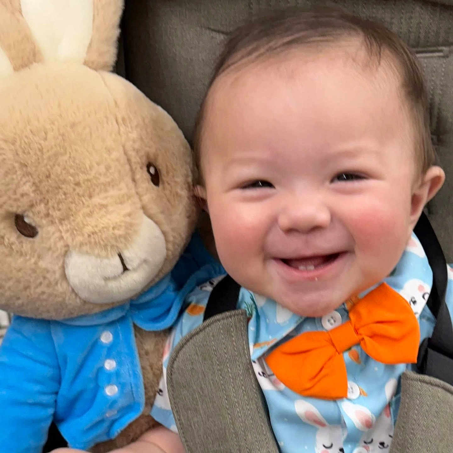 Ezekiel is registered to the contest to win money with this photo: baby, smiling, child, plush_toy, stuffed_animal, bunny, orange_bow_tie, blue_shirt, car_seat, happy, cute, indoor, infant, face, person, clothing, toy, seatbelt, closeup, portrait