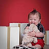 Ezekiel is registered to the contest to win money with this photo: baby, candid, child, cute, floor, gift_box, happy, indoor, mohawk, playful, plush_toy, portrait, red_background, shirt, shorts, sitting, smiling, sneakers, stuffed_animal, toy