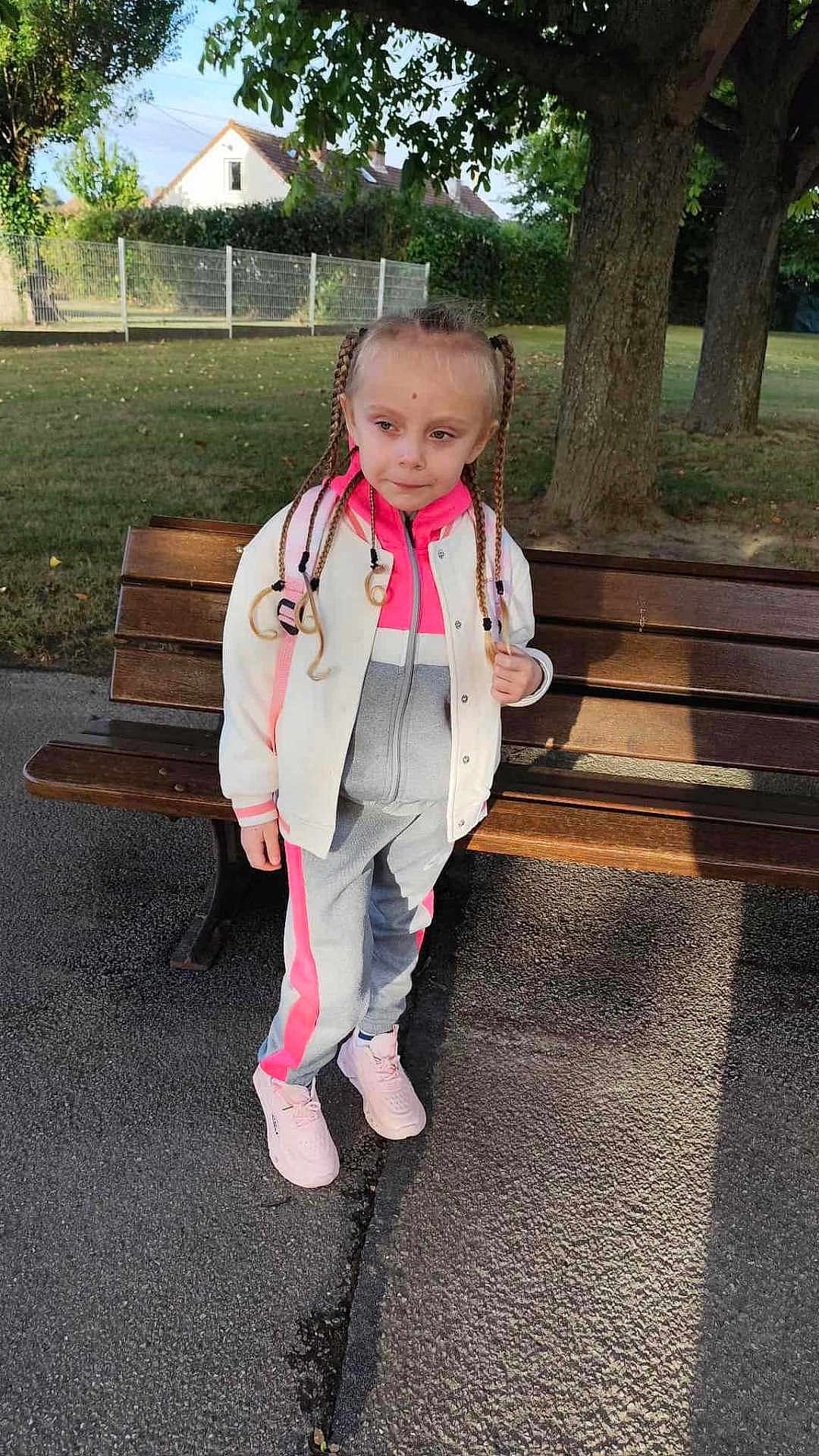 Lyana participe au concours pour gagner de l'argent avec cette photo : child, braids, park, bench, outdoor, grass, tree, sidewalk, jacket, tracksuit, sneakers, daylight, young, person, casual_clothing, nature, quiet, standing, shoes, portrait