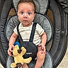 baby, infant, child, stuffed_animal, pacifier, baby_seat, cushion, onesie, animal_print, blue_pacifier, plush_toy, barefoot, looking_at_camera, curious_expression, indoors, seatbelt, black_straps, soft_toy, floor_tile, person