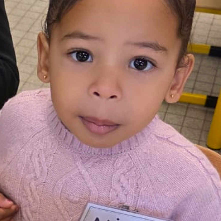 Nila a rejoint le concours — aidez-le/la à gagner de superbes lots ! bun, child, classroom, curly_hair, cute, education, face, girl, indoor, learning, name_tag, person, pink, play, seat, sweater, table, toy, wooden_blocks, young