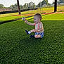 baby, child, baseball, sportswear, grass, turf, outdoor, playing, happy, sitting, sunlight, smiling, socks, suspenders, field, netting, daytime, recreation, fun, joyful