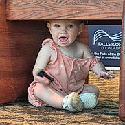 Ahna joined the competition — help win amazing prizes! baby, child, romper, sitting, carpet, wooden_table, indoor, happy, curious, person, footwear, shoe, smile, expression, playful, small_object, furniture, floor, candid, young