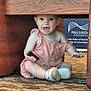 baby, child, romper, sitting, carpet, wooden_table, indoor, happy, curious, person, footwear, shoe, smile, expression, playful, small_object, furniture, floor, candid, young