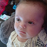 Dravyn is registered to the contest to win money with this photo: baby, child, face, portrait, curly_hair, onesie, animal_print, indoor, cushion, hand, comfort, expression, young_child, soft_light, close_up, person, infant, home, relaxing, cute