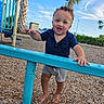 toddler, child, playground, barefoot, smiling, curly_hair, blue_shirt, shorts, metal_bar, wood_chips, outdoor, daylight, palm_trees, sky, fence, park, happy, person, play, summer