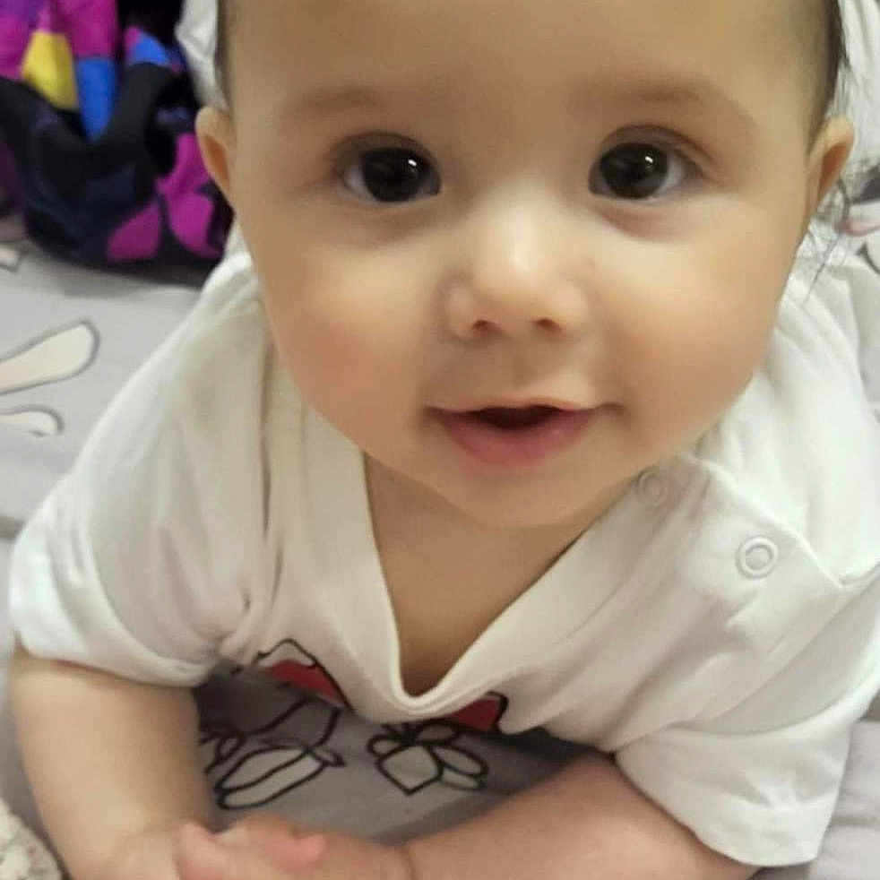 Taline a rejoint le concours — aidez-le/la à gagner de superbes lots ! baby, infant, child, cute, hands, bedspread, floral_pattern, clothing, white_shirt, face, eyes, laying_down, indoors, blanket, soft_lighting, portrait, smiling, skin, head, young