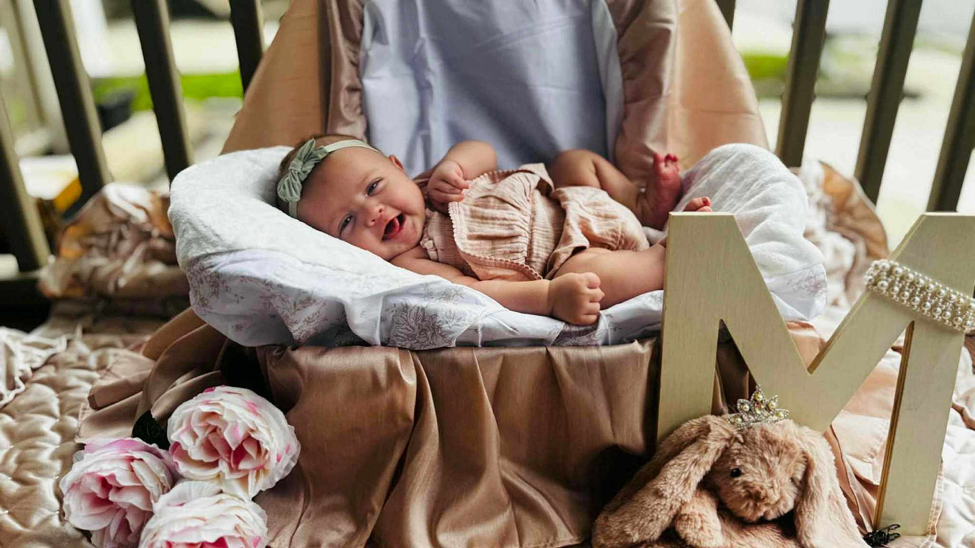 Maybel is registered to the contest to win money with this photo: baby, smiling, headband, basket, cushion, plush_toy, bunny, flowers, pink, soft_fabric, portrait, indoor, cute, child, decor, toy, happy, infant, cozy, photography