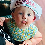Makai is registered to the contest to win money with this photo: baby, infant, child, face, hat, krispy_kreme, doughnuts, chocolate, tongue, patterned_clothing, cute, curious, blue_eyes, hand, person, portrait, colorful, soft_lighting, indoor, holding