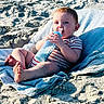 Makai is registered to the contest to win money with this photo: baby, bottle, milk, towel, sand, beach, child, onesie, striped_clothing, foot, hand, sunlight, relaxing, infant, cute, person, outdoor, skin, face, lying_down