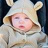 baby, child, blue_eyes, knitted_hoodie, beige_clothing, hood_with_ears, stroller, close_up, cute, portrait, infant, face, buttoned_sweater, warm_clothing, outdoor, soft_lighting, young_child, candid, expression, cozy