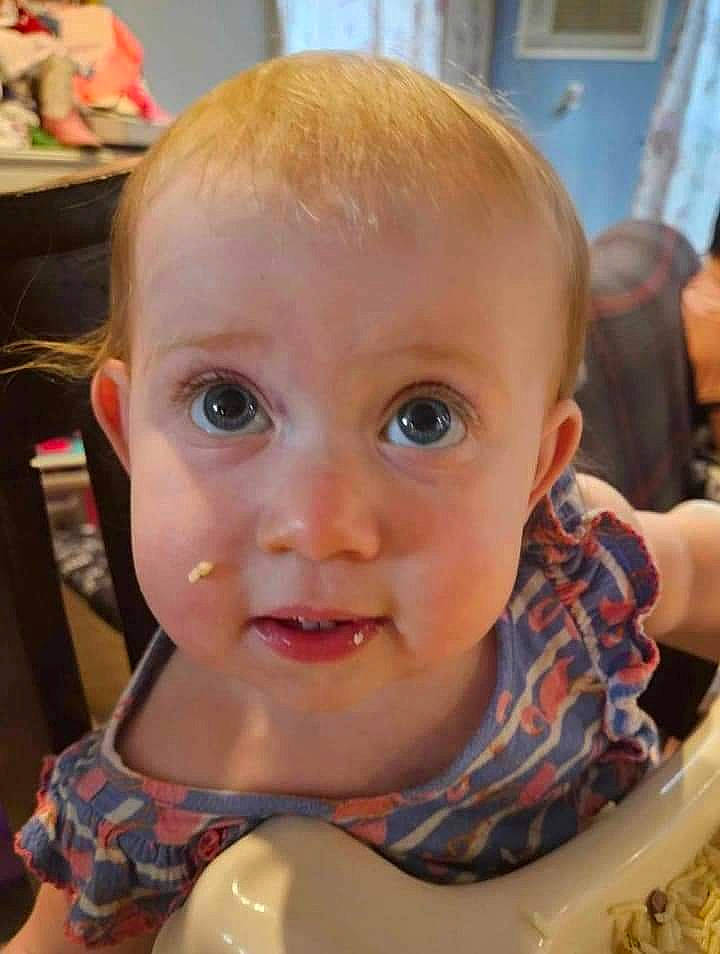 Mercy is registered to the contest to win money with this photo: baby, baby_playing_with_food, baby_toddler_clothing, bib, chair, cheek, child, comfort_food, dishware, drinkware, eyelash, fun, happy, person, serveware, sitting, smile, surprise, sweetness, tableware