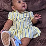 baby, child, dress, yellow, striped, blue_bow, blue_sandals, couch, brown_couch, sitting, curious, indoors, plush, comfortable, small_child, person, cute, adorable, young, portrait