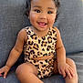toddler, child, smiling, sitting, leopard_print, curly_hair, couch, indoors, happy, person, barefoot, skin, face, clothing, furniture, portrait, cute, young_child, seat, cozy