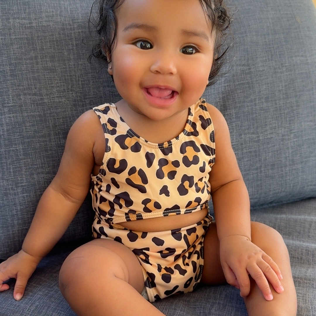 Jia is registered to the contest to win money with this photo: barefoot, child, clothing, couch, cozy, curly_hair, cute, face, furniture, happy, indoors, leopard_print, person, portrait, seat, sitting, skin, smiling, toddler, young_child