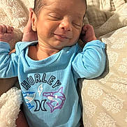 Alexander Appolo is registered to the contest to win money with this photo: baby, baby_clothes, blanket, blue_onesie, clothing, cozy, cute, face, hand, head, human, indoor, infant, newborn, portrait, resting, skin, sleeping, smile, soft