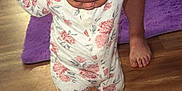 Amari is registered to the contest to win money with this photo: toddler, child, floral_onesie, walking, hand_holding, wooden_floor, purple_rug, curly_hair, tattoo, adult_hand, barefoot, indoor, baby, person, home, support, phone, flooring, foot, learning_to_walk