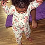 toddler, child, floral_onesie, walking, hand_holding, wooden_floor, purple_rug, curly_hair, tattoo, adult_hand, barefoot, indoor, baby, person, home, support, phone, flooring, foot, learning_to_walk