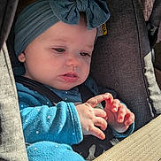 Allison is registered to the contest to win money with this photo: baby, child, car_seat, blue_headband, bow, blue_clothing, seatbelt, hands, curious, portrait, infant, cute, indoor, closeup, person, young_child, sitting, safety, face, expression