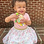 toddler, child, smiling, plush_toy, pink_shirt, floral_skirt, brick_wall, brick_steps, happy, outdoor, person, cute, baby, sitting, playful, young_child, daylight, casual_clothing, portrait, candid