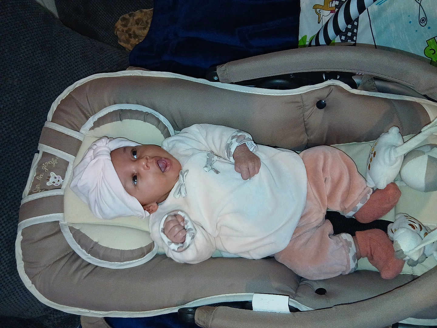 Hawa participe au concours pour gagner de l'argent avec cette photo : baby, infant, baby_carrier, turban_hat, pink_clothing, white_clothing, soft_toys, blanket, cushion, indoor, cozy, cute, child, sleepwear, footwear, expression, person, lying_down, comfort, warm