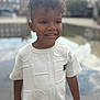 child, boy, smiling, curly_hair, white_shirt, outdoor, urban, reflection, water, face, happy, portrait, standing, short_sleeves, daylight, casual_clothing, young, people, background_blur, fashion