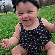 Bella is registered to the contest to win money with this photo: baby, infant, child, smile, grass, headband, bow, park, outdoor, sitting, onesie, chubby_legs, hand, face, portrait, happy, candid, green_grass, trees, cute