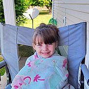 Zoey is registered to the contest to win money with this photo: child, girl, blanket, dinosaur_pattern, chair, outdoor, porch, smiling, greenery, tree, satellite_dish, casual_clothing, happy, hair_bangs, daylight, fabric, relaxing, seated, patterned_pants, nature