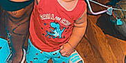 Justin is registered to the contest to win money with this photo: adult, casual, child, curious, flooring, furniture, hand_holding, home, indoor, person, red_tank_top, shoes, shorts, slippers, standing, tattoo, toddler, toy, wide_eyes, wooden_floor