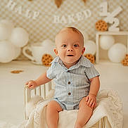 Kashtyn joined the competition — help win amazing prizes! baby, child, infant, smiling, blue_clothing, striped_shirt, wooden_bed, blanket, white_blanket, balloons, decorations, banner, cookie_prop, celebration, milestone, studio_photo, portrait, happy, cute, indoor