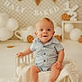 baby, child, infant, smiling, blue_clothing, striped_shirt, wooden_bed, blanket, white_blanket, balloons, decorations, banner, cookie_prop, celebration, milestone, studio_photo, portrait, happy, cute, indoor