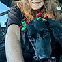 black_dog, car_interior, close_up, dog, freckled_skin, glasses, hair, happy, long_hair, passenger, pet, portrait, red_and_green_bows, ribbon_bows, seatbelt, selfie, smile, tongue_out, window, woman