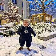 Adam participe au concours pour gagner de l'argent avec cette photo : child, toddler, snow, winter_clothing, hat, boots, snowy_park, trees, bench, urban, evening, street_lights, snow_covered, playful, cute, cold_weather, outdoor, person, warm_clothing, nature