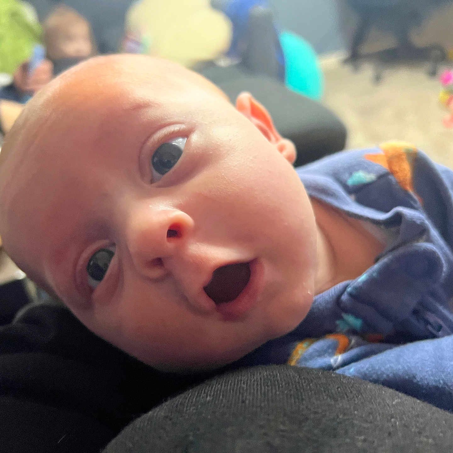 Grayson is registered to the contest to win money with this photo: baby, blue_clothing, blurred_background, candid, carpet, child, close_up, cozy_room, cute, expression, face, head, indoor, infant, newborn, open_mouth, person, portrait, soft_lighting, toy