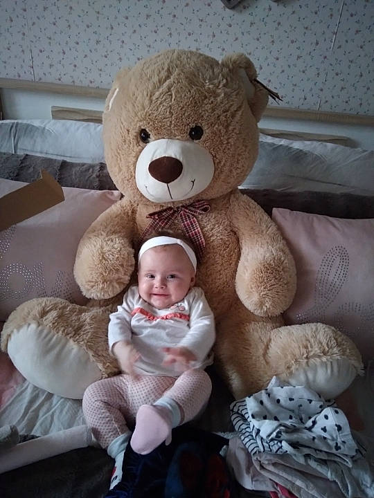 Camille a rejoint le concours — aidez-le/la à gagner de superbes lots ! baby, child, comfort, couch, fur, happy, head, joy, linens, nose, person, pink, plush, room, sitting, skin, smile, stuffed_toy, teddy_bear, toddler
