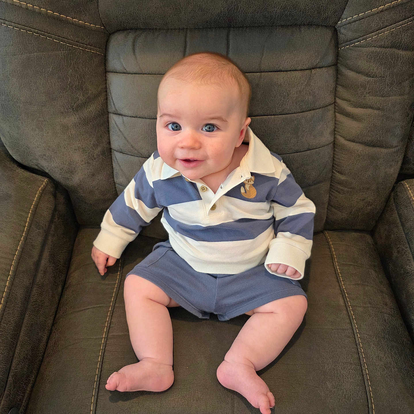 Malakhi is registered to the contest to win money with this photo: baby, child, infant, blue_eyes, striped_shirt, polo_shirt, shorts, smile, sitting, leather_chair, furniture, indoor, cute, portrait, person, human, young, skin, legs, feet
