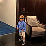 Daniel participe au concours pour gagner de l'argent avec cette photo : armchair, blue_shirt, carpet, casual, child, cushion, fashion, floor, indoor, no_smoking_sign, person, room_numbers, shoes, shorts, socks, standing, sunglasses, toddler, wall, wood_panel