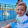 adult, background, blue_eyes, child, daylight, hair, happy, outdoor, person, railing, sailboats, seated, shorts, sky, smile, sunny, toddler, tshirt, vacation, water
