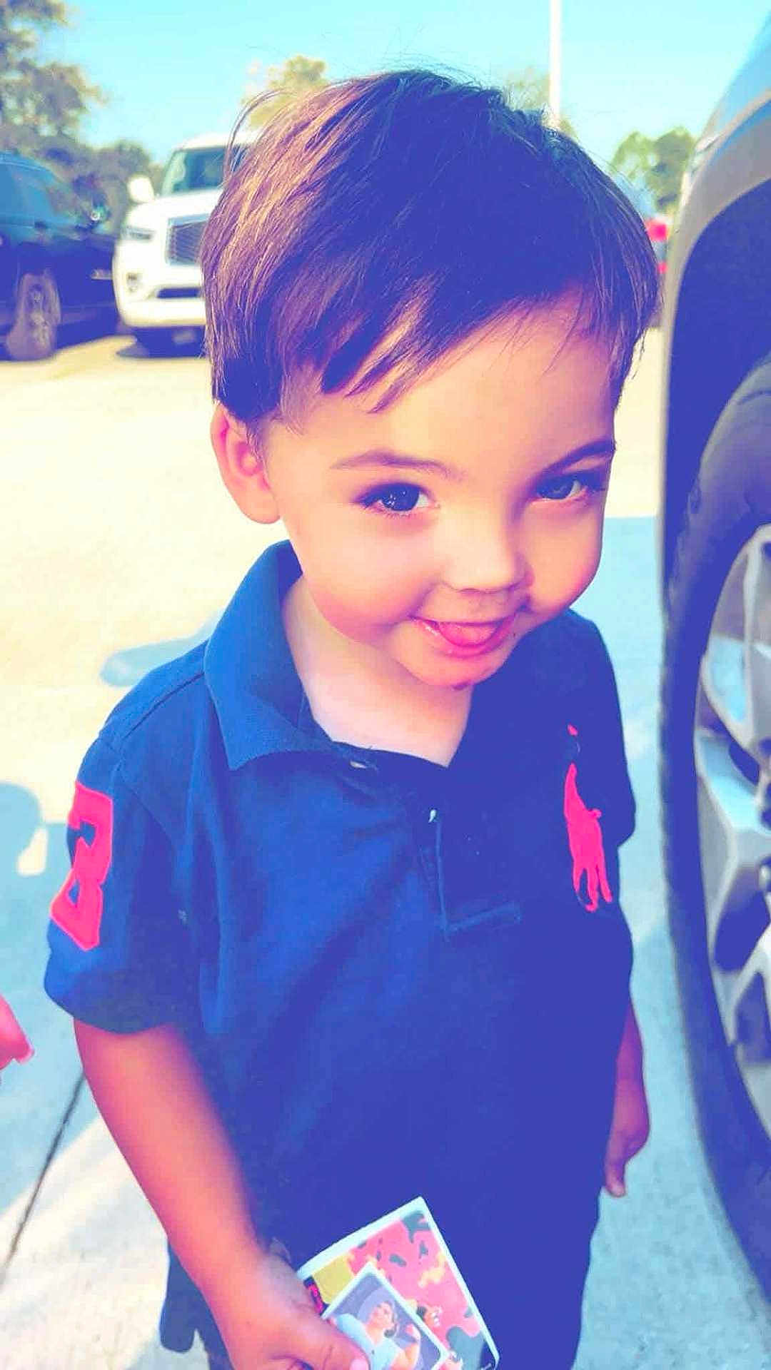 Jerimach is registered to the contest to win money with this photo: child, boy, smile, blue_shirt, outdoor, daylight, cars, parking_lot, holding_card, short_hair, young, face, cheeky, tongue_out, casual_clothing, polo_shirt, sunlight, happy, person, portrait