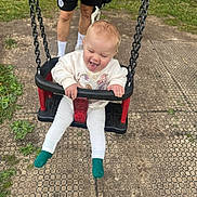 Avery is registered to the contest to win money with this photo: adult, child, clothing, daytime, dog, fence, fun, grass, happy, joy, nature, outdoor, person, play, playground, rubber_tiles, smiling, socks, swing, toddler