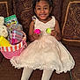 child, girl, smiling, dress, white_tights, pink_shoes, couch, basket, toys, eggs, hair_bow, beads, indoor, happy, portrait, face, furniture, home, celebration, easter_eggs
