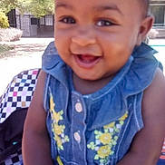Royce'Lynn is registered to the contest to win money with this photo: baby, child, smiling, happy, denim_dress, yellow_flowers, holding_hands, outdoor, sunny, trees, building, person, portrait, infant, cute, dimples, seat, checkered_pattern, skin, young