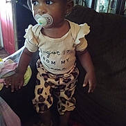 Royce'Lynn is registered to the contest to win money with this photo: toddler, child, pacifier, headband, leopard_print, clothing, shirt, pants, sandals, couch, living_room, furniture, door, person, baby, indoor, portrait, standing, cute, home