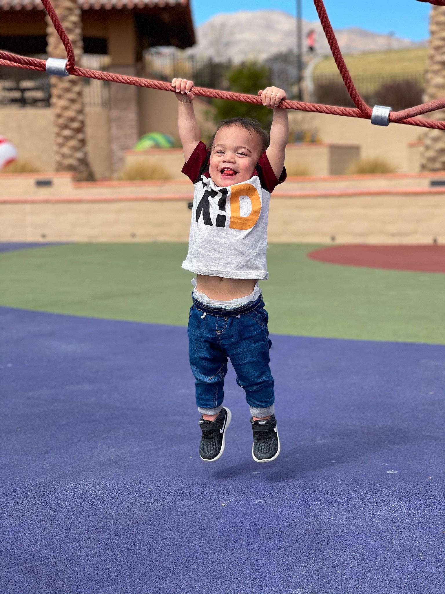 Rhett is registered to the contest to win money with this photo: child, city, denim, electric_blue, fun, gesture, grass, happy, landscape, leg, leisure, outdoor_play_equipment, person, recreation, sky, smile, swing, t_shirt, toddler, tree