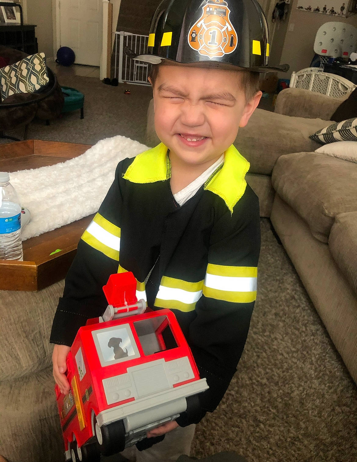 Joshua Jr. is registered to the contest to win money with this photo: bottle, carmine, emergency_service, event, firefighter, headgear, headwear, high_visibility_clothing, machine, motor_vehicle, person, personal_protective_equipment, room, service, smile, tire, toddler, toy_vehicle, uniform, water_bottle