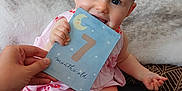 Judith a rejoint le concours — aidez-le/la à gagner de superbes lots ! baby, infant, child, milestone_card, 7_months_old, pink_dress, couch, blanket, hand, indoor, smiling, happy, cute, face, legs, feet, skin_mark, person, sitting, home