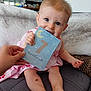 baby, infant, child, milestone_card, 7_months_old, pink_dress, couch, blanket, hand, indoor, smiling, happy, cute, face, legs, feet, skin_mark, person, sitting, home