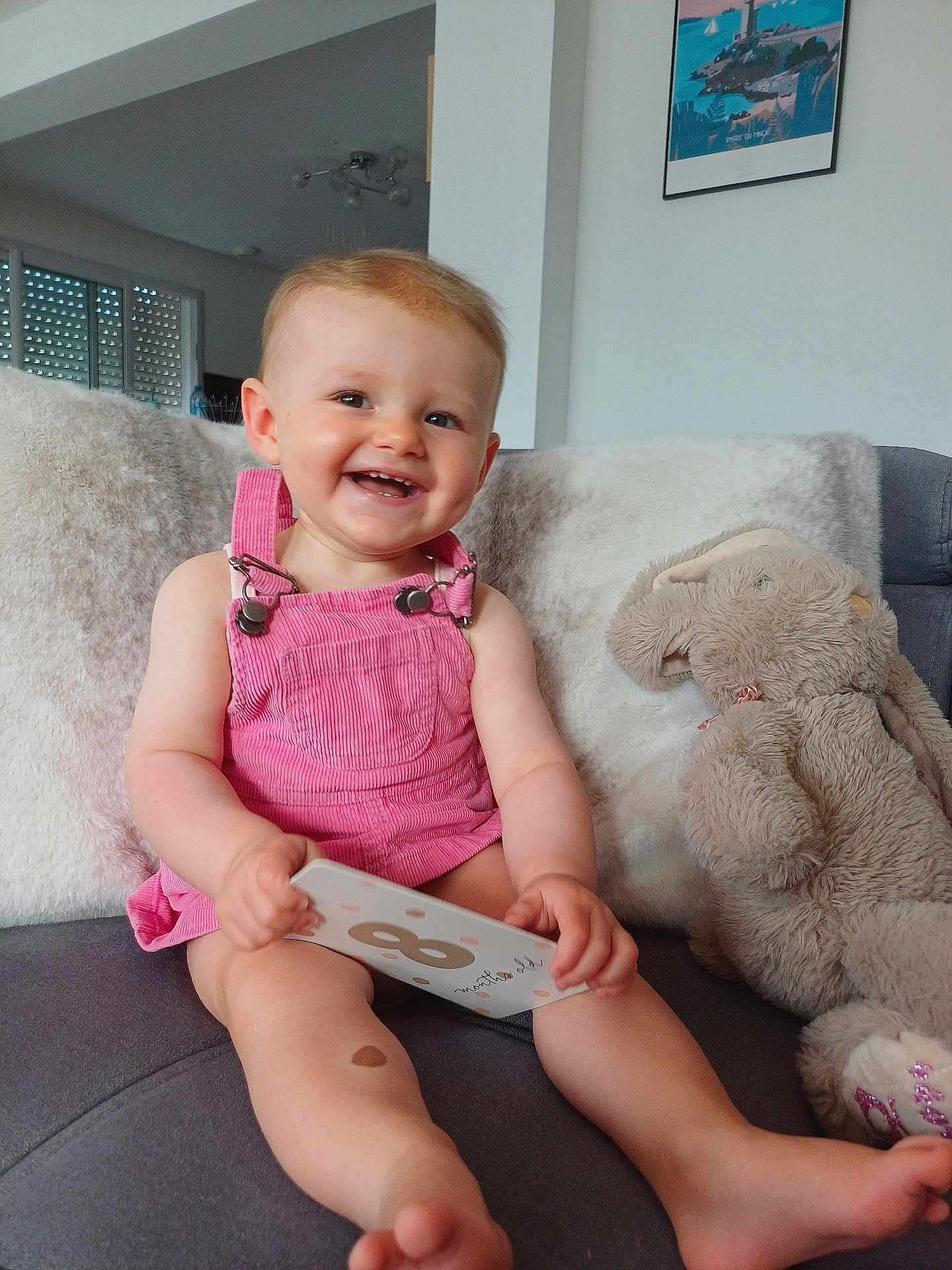 Judith a rejoint le concours — aidez-le/la à gagner de superbes lots ! baby, child, smiling, pink_overalls, plush_toy, bunny, couch, indoor, happy, infant, card, furniture, home, person, portrait, cute, sitting, soft_toy, living_room, cozy