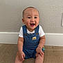 baby, child, smiling, sitting, blue_overalls, white_shoes, wooden_floor, indoor, happy, cute, person, infant, short_hair, casual_clothing, wall, floor, footwear, young_child, one_person, portrait